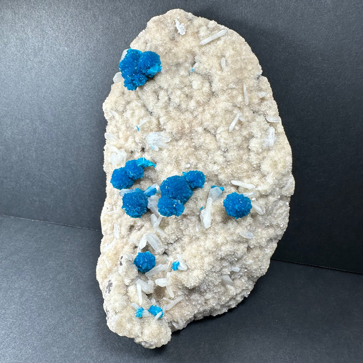 Cavansite and stilbite on pale rock with larger bright blue clusters and clear crystals
