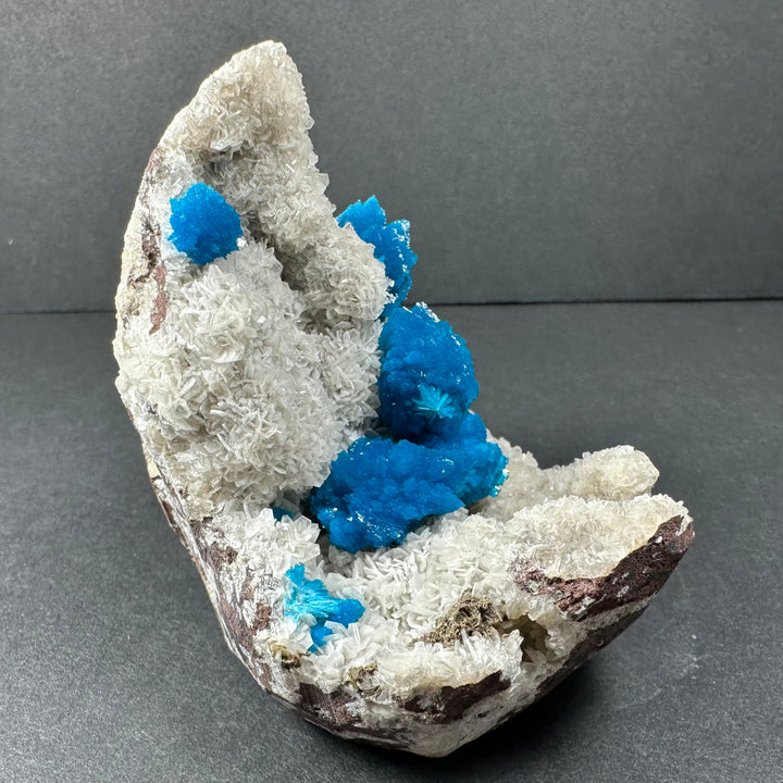Angled mineral specimen with white crystal shelves and scattered bright blue crystal points