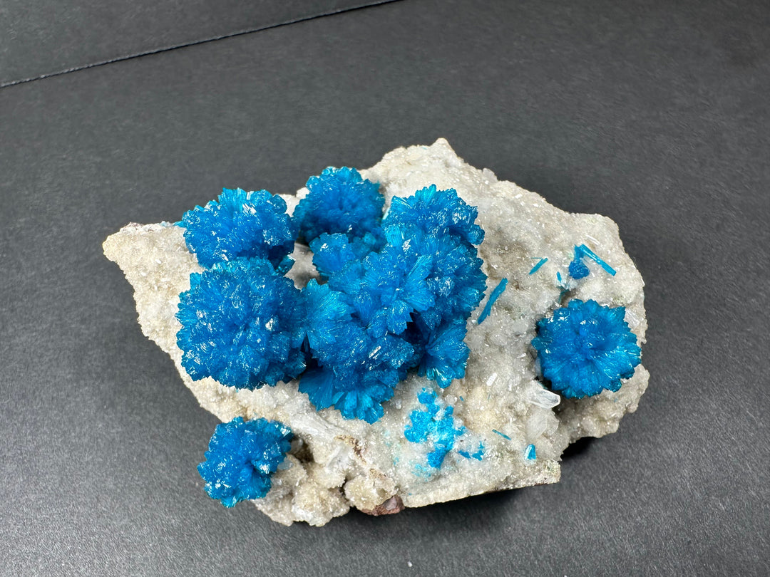 Cavansite and stilbite crystal cluster on light beige rock matrix with bright blue points