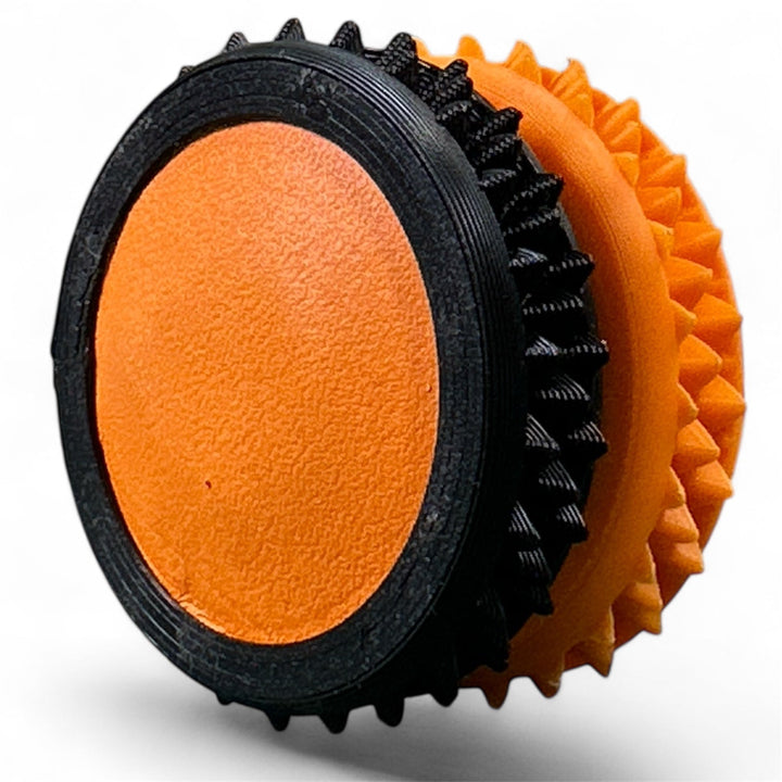 Black and orange fidget gear with textured rings and oval center pad