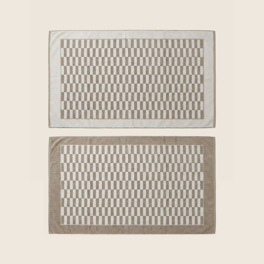 Pair of beige and white checkered bath towels with border, laid flat