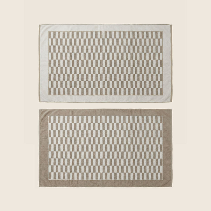 Pair of beige and white checkered bath towels with border, laid flat