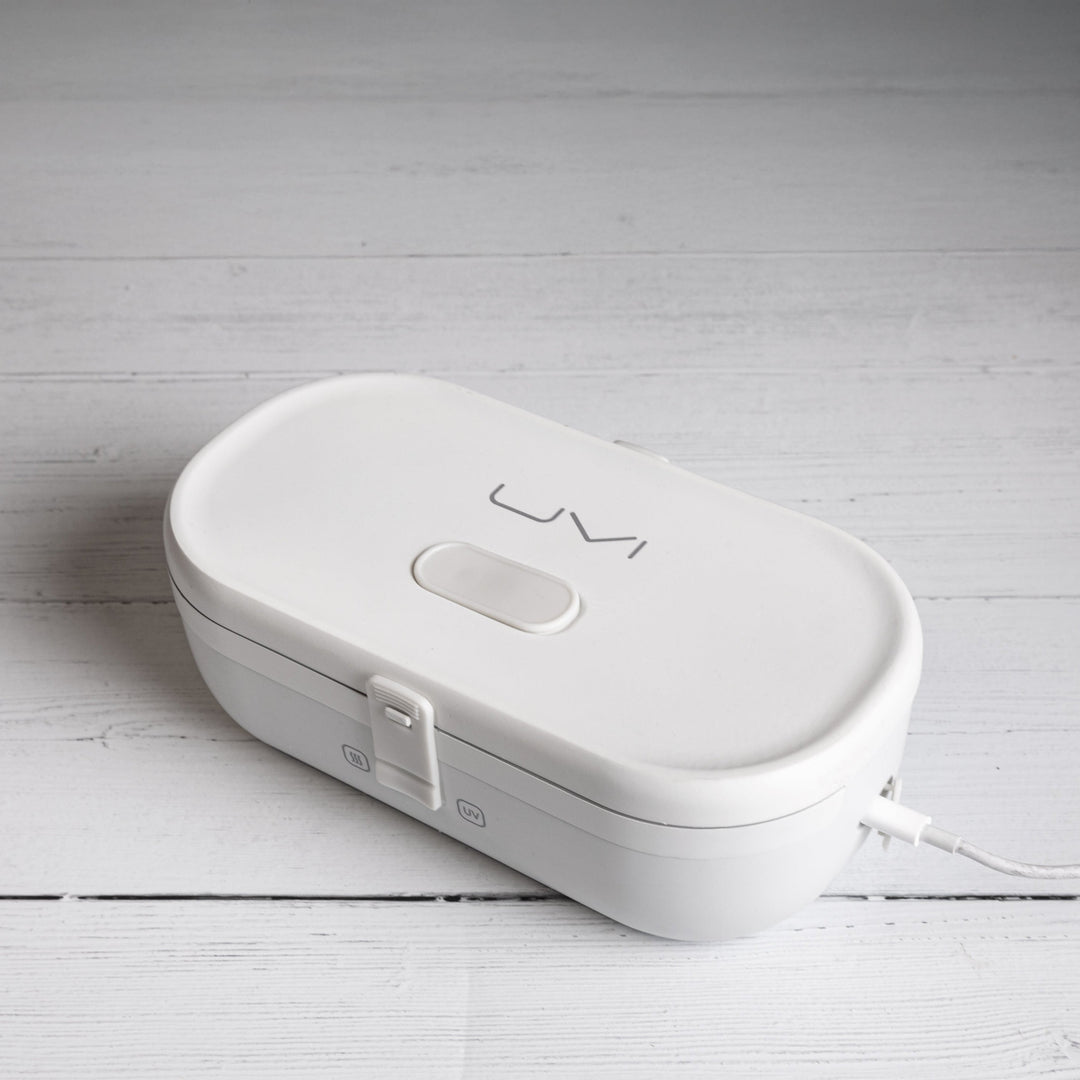 Closed white self-heating lunch box with front heating controls and side charging port.