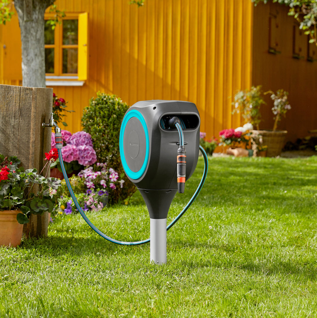 Gray roll-up garden hose reel with blue ring near flower pots and connected hose