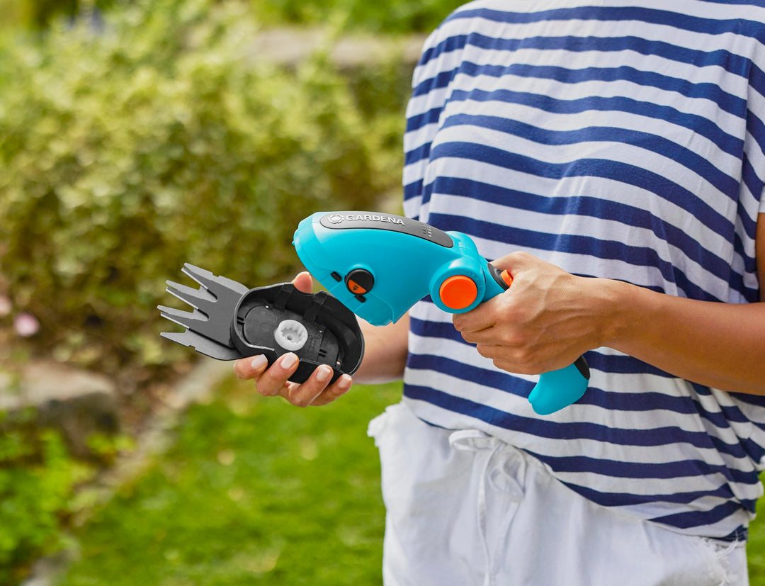 Handheld teal cordless shears with orange trigger, cutting shrub tops