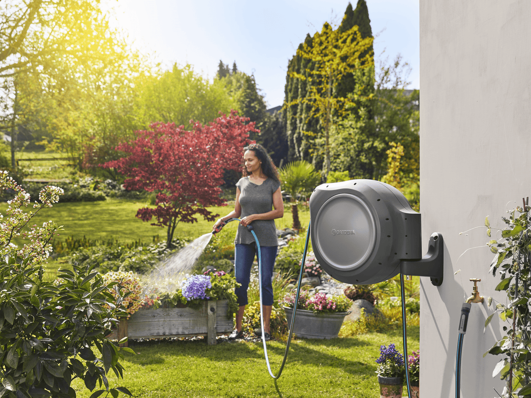 Retractable hose reel with gray drum mounted on wall, woman watering garden