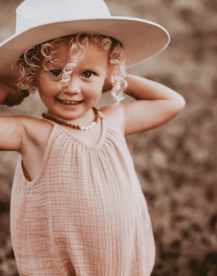 Raw amber beaded necklace with moonstone accents on a smiling child in a hat