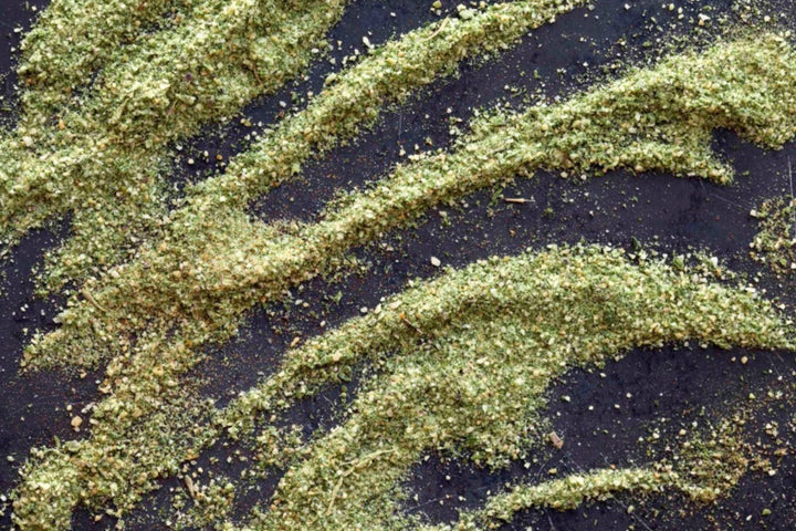 Green herb seasoning granules on dark background with diagonal stripes