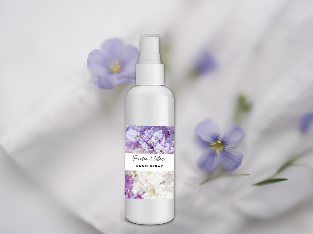 Room spray bottle with white pump on white fabric beside purple flowers