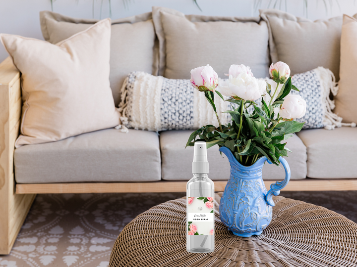 Room spray bottle with white pump on a table next to a blue vase with flowers
