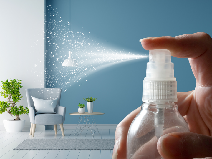 Hand holding a room spray bottle while mist sprays into a room