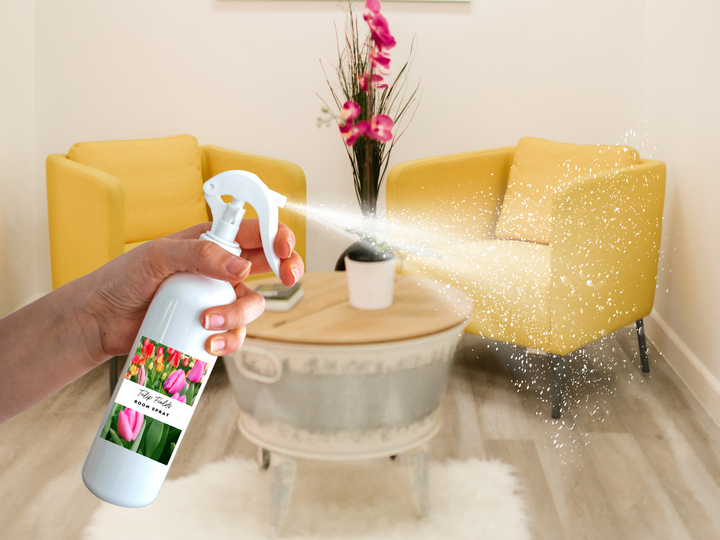 Hand holding room and linen spray bottle with trigger, mist dispersing from nozzle