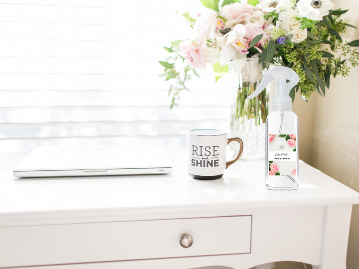 Room and linen spray bottle with trigger nozzle, placed near flowers and a mug