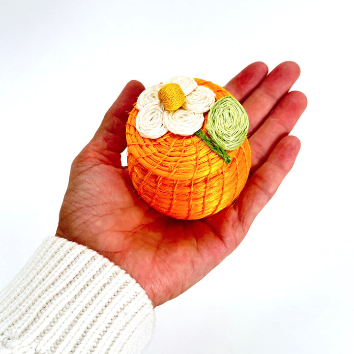 Orange round woven tiny basket with daisy-style flowers, held in a person’s open hand.