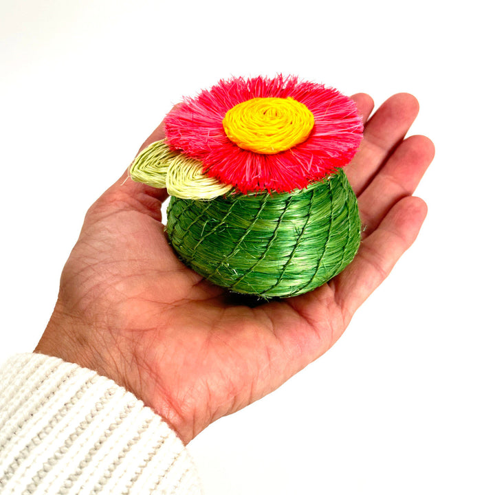 Tiny woven basket in a hand, green base with red fringed flower and yellow center.