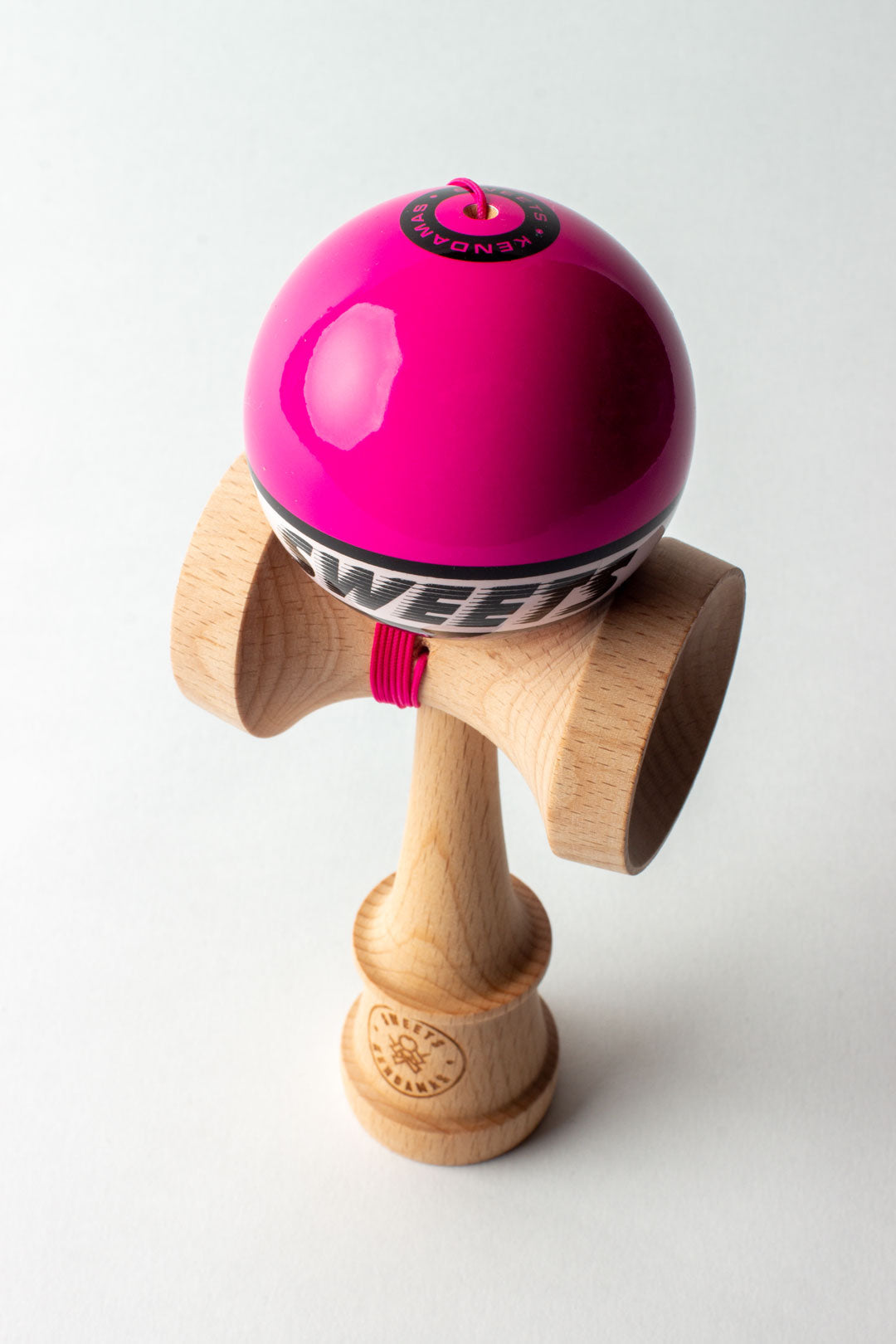 Wooden kendama with glossy pink ball and red string, side view