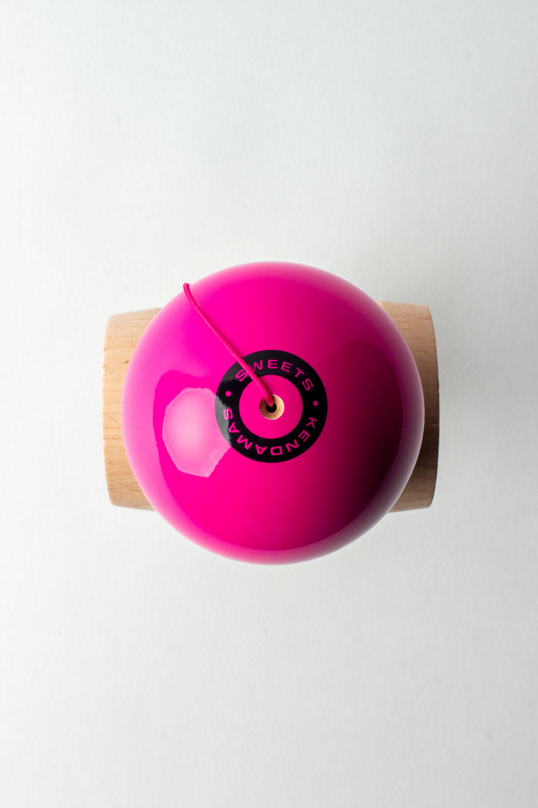 Wooden kendama top view: glossy pink ball with black center cap