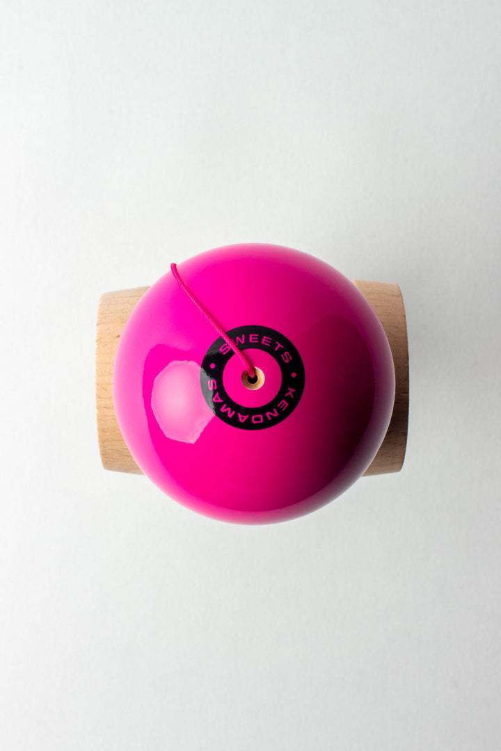 Wooden kendama top view: glossy pink ball with black center cap