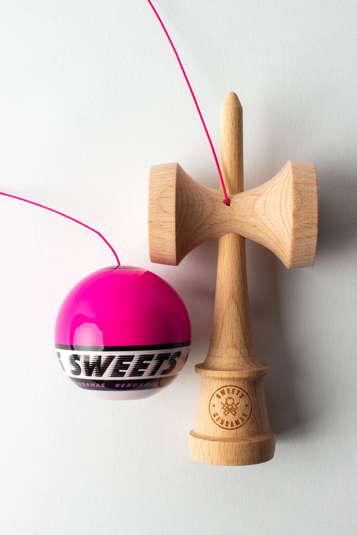 Wooden kendama with pink ball and red laces, ball-on-base pose