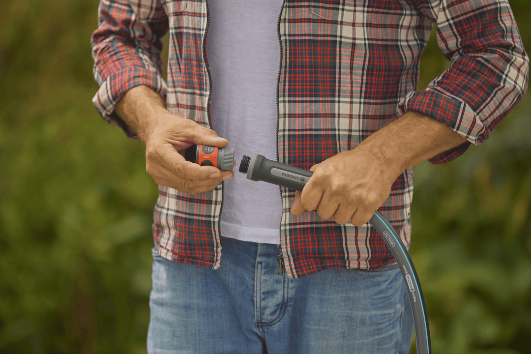 Person holding a garden hose nozzle with blue stripe hose and dark coupling parts