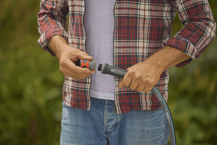 Person holding a garden hose nozzle with blue stripe hose and dark coupling parts