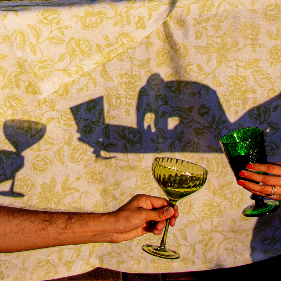 Ribbed sage-green coupe glass raised in celebration by a person holding the stem.