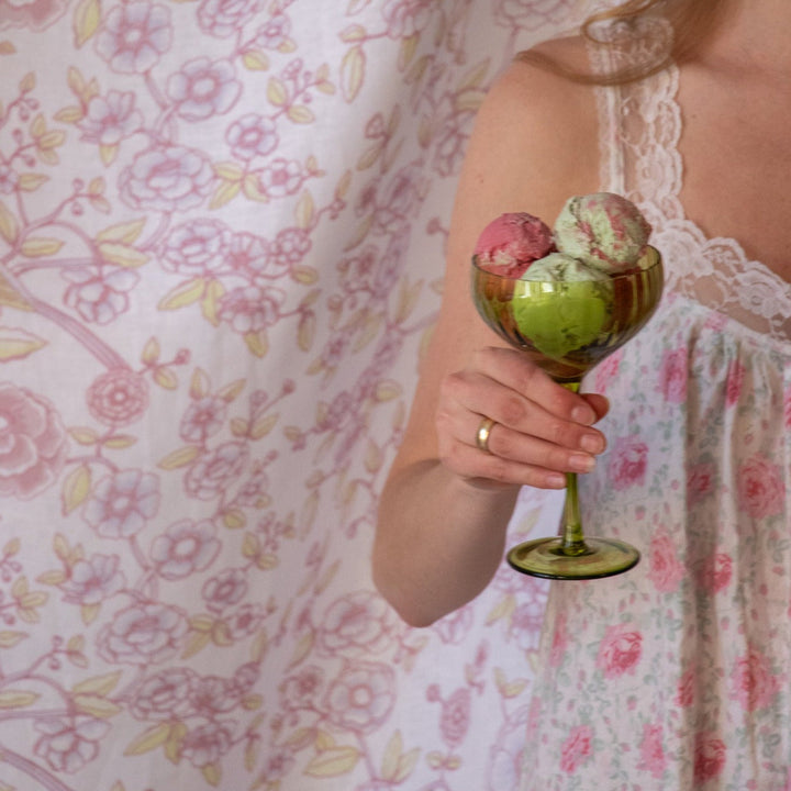 Ribbed sage-green coupe glass with ice cream, held in front of floral fabric.
