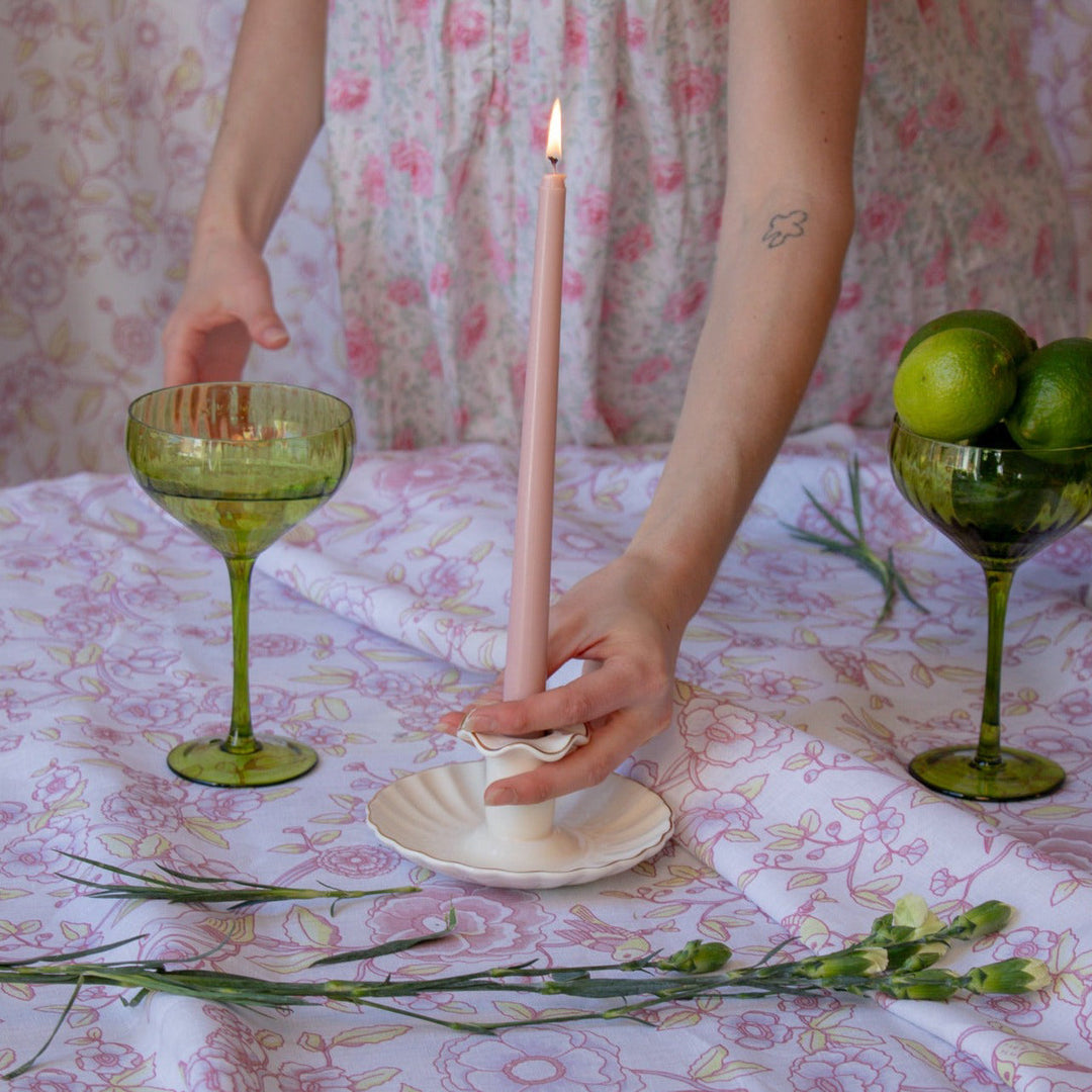 Ribbed sage-green coupe glasses on table while a person lights a candle between them.