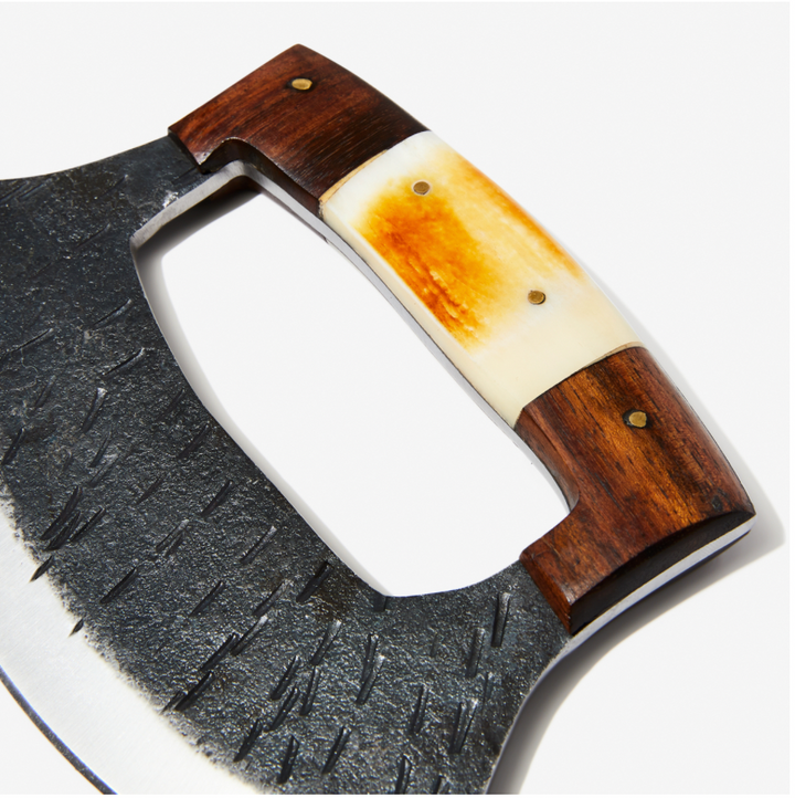 Close-up ULU knife: textured steel crescent blade with wood handle and amber inlay