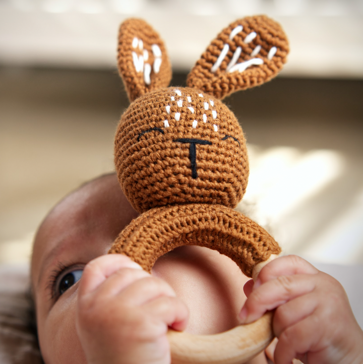 Bunny-shaped crochet rattle teether with wooden ring, brown with white stitched details