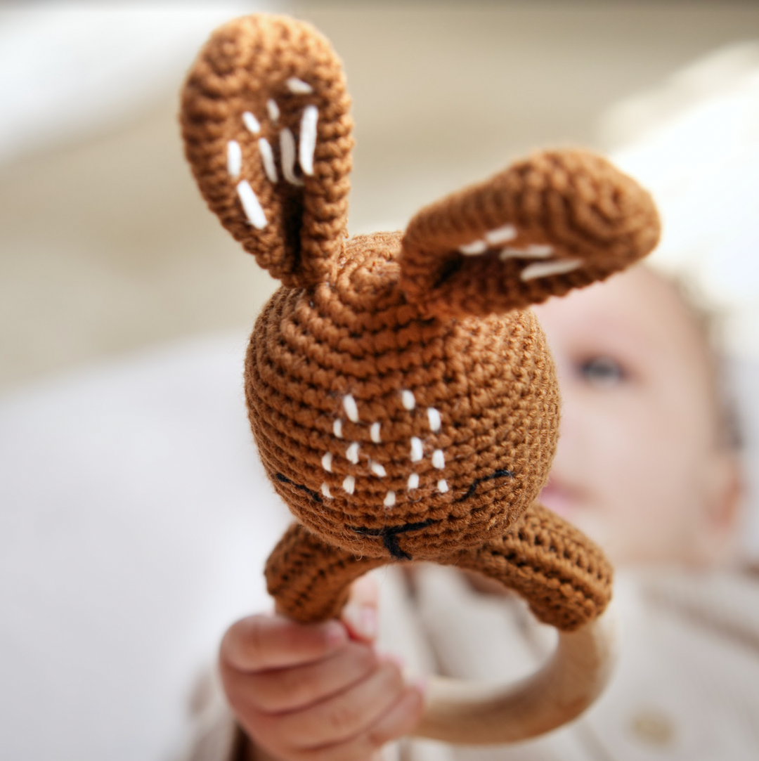 Brown bunny crochet rattle teether with wooden ring, held in a baby's hands