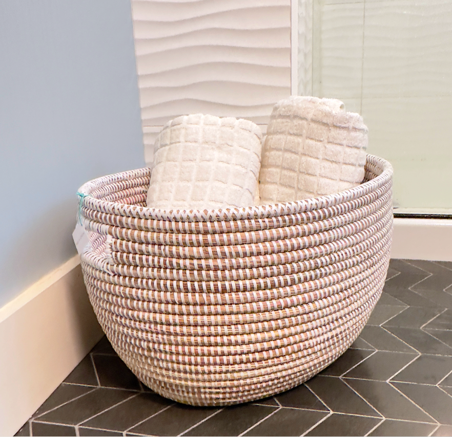 Woven oval basket filled with folded white towels and a soft pink top