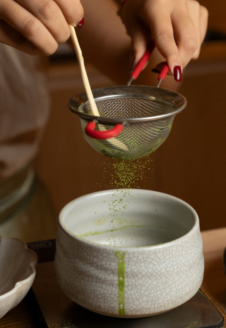 Single-cultivar matcha powder sifted into a ceramic bowl, with bamboo whisk beside