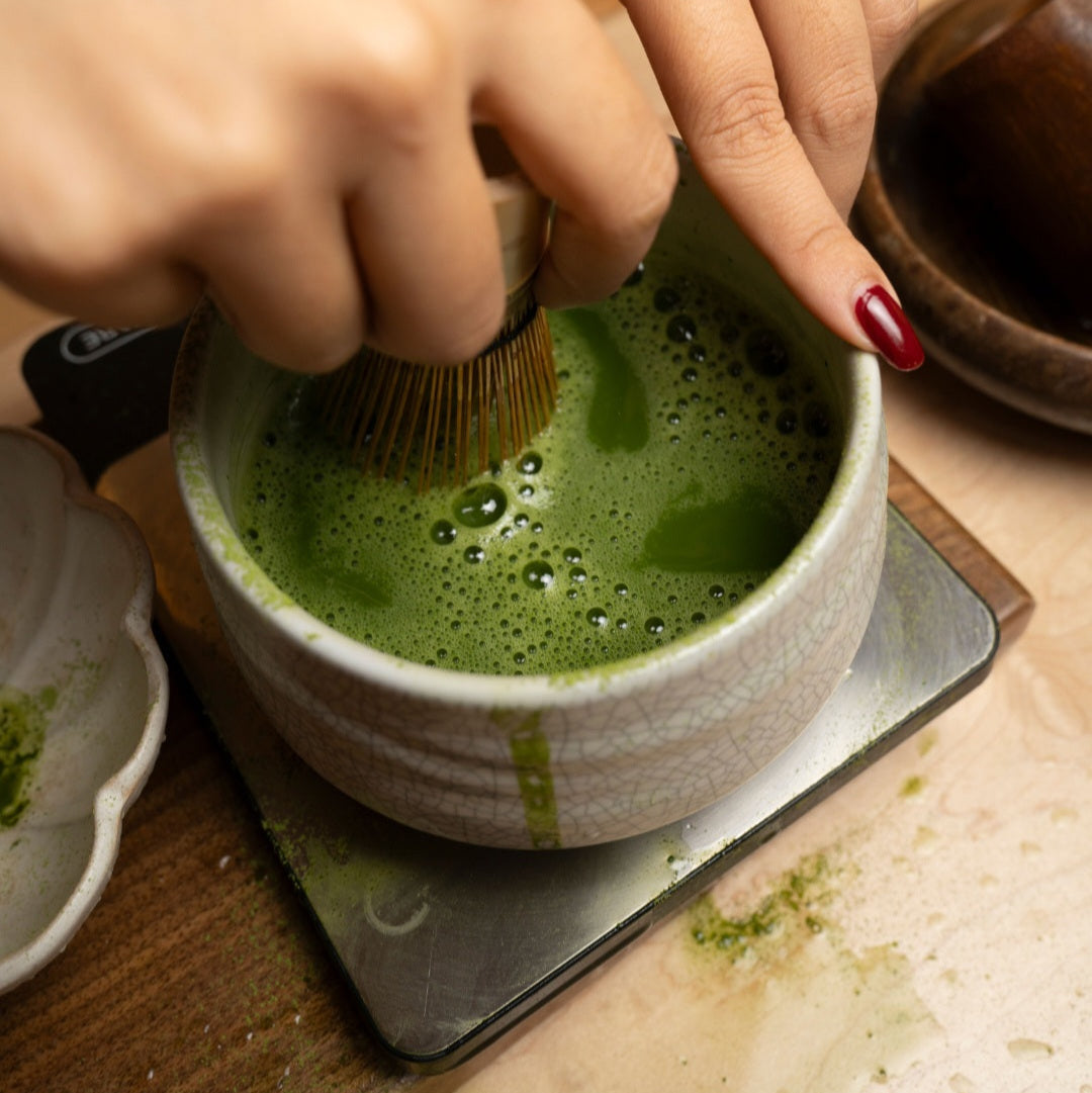 Ceramic bowl of green matcha whisked with bubbles, tray with tea tools