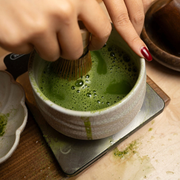 Ceramic bowl of green matcha whisked with bubbles, tray with tea tools
