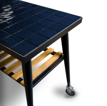 Outdoor grill cart with blue tiled tabletop and lower storage grate on wheeled legs