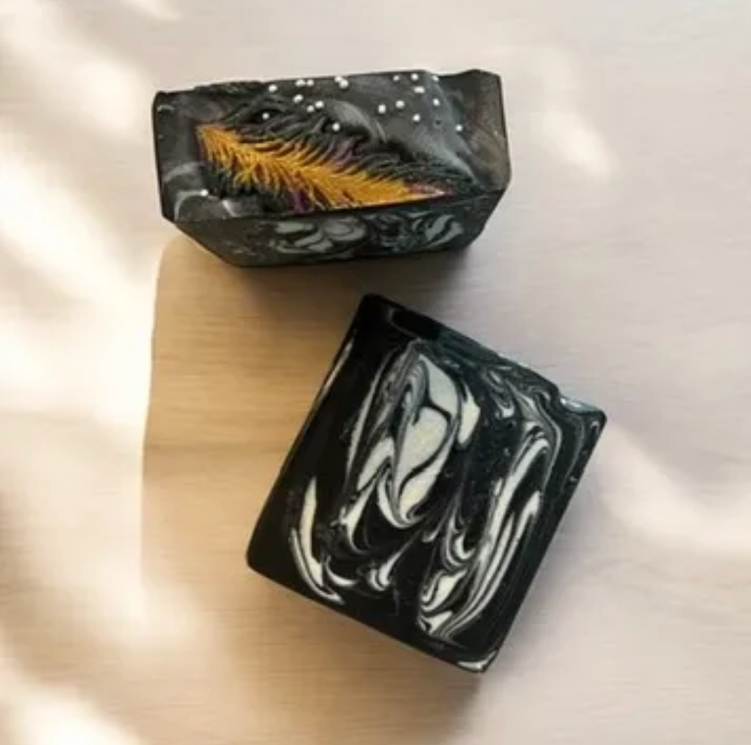Handmade black soap bar with amber palm-frond design, marbled white swirls
