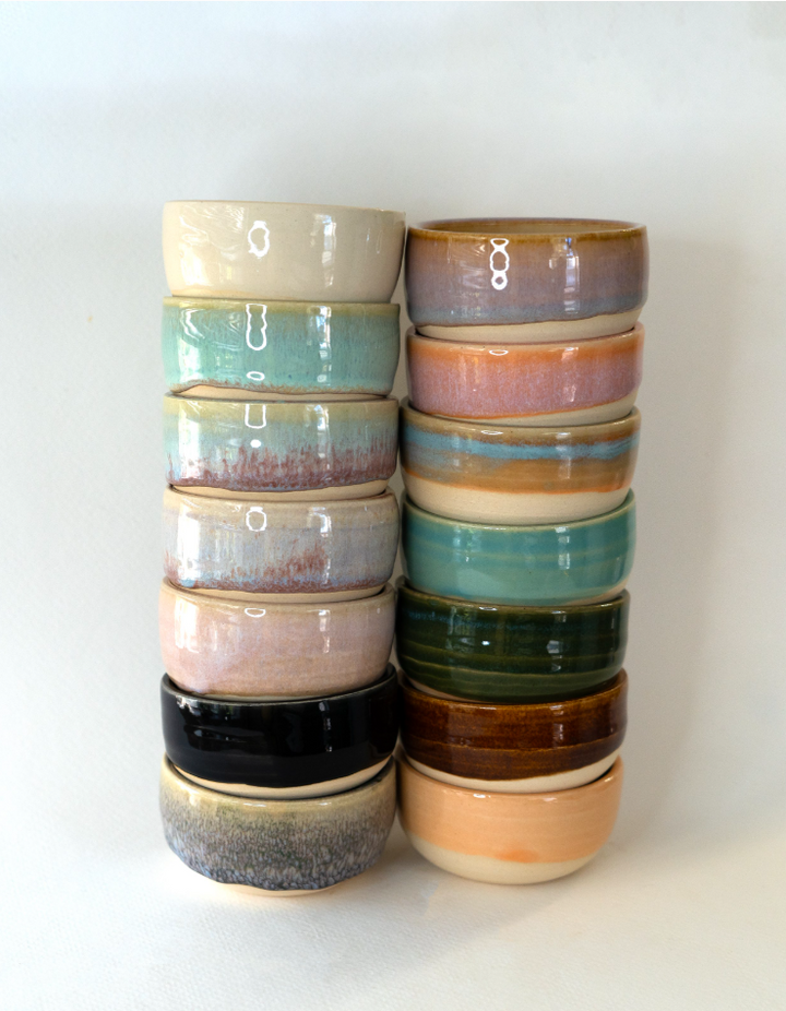 Stack of ceramic condiment cups in assorted glaze colors, including black and teal