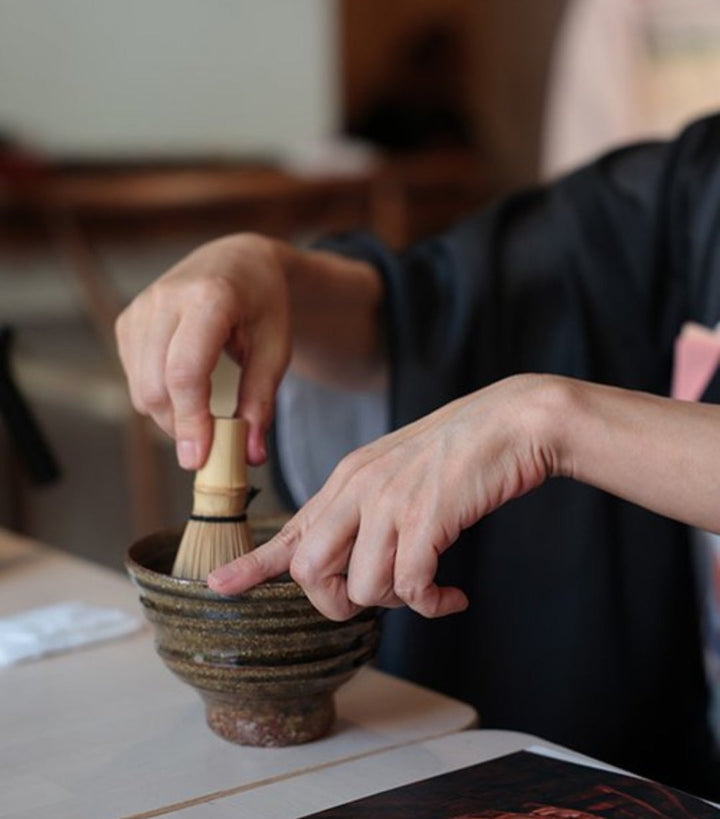Single-cultivar matcha bowl with bamboo whisk and hands preparing to whisk