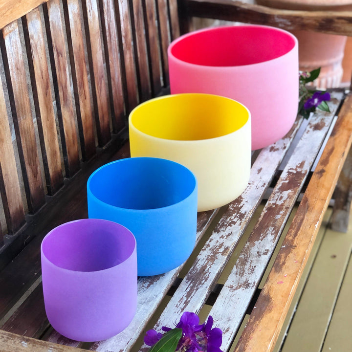Set of 4 colorful sound bowls: pink, yellow, blue, and purple on wooden floor