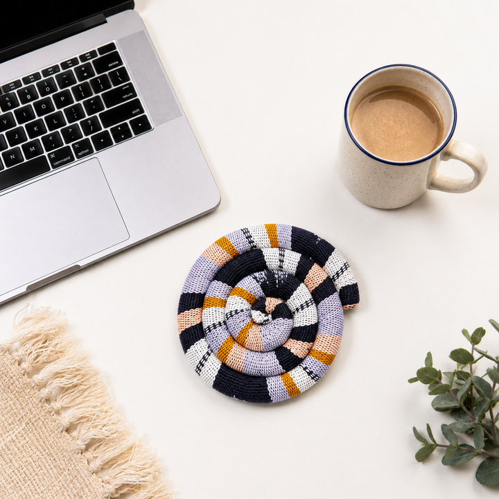 Round spiral trivet with navy and cream plaid stripes, orange accents, and rosette center
