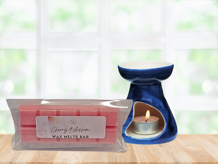 Blue ceramic wax warmer with lit tealight beside clear-wrapped cherry blossom wax melt bar
