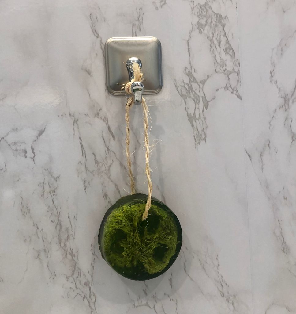 Dark green round soap bar attached to tan rope hanging from a wall hook