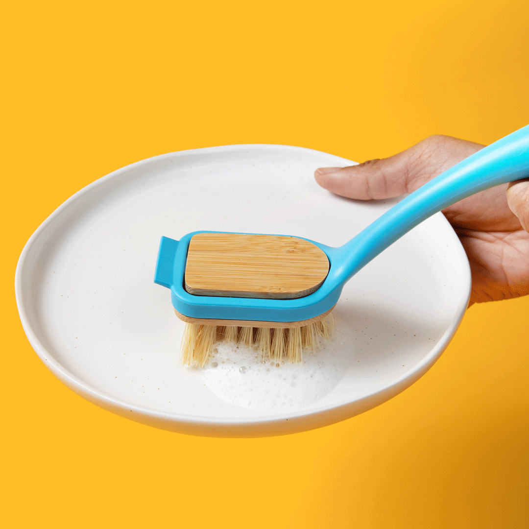 Dish brush held over a plate with yellow bristles and blue handle