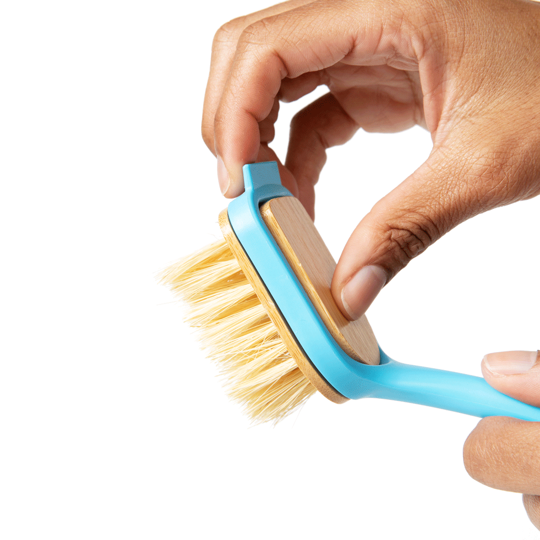 Hand holding dish brush, blue handle with angled wooden insert and yellow bristles