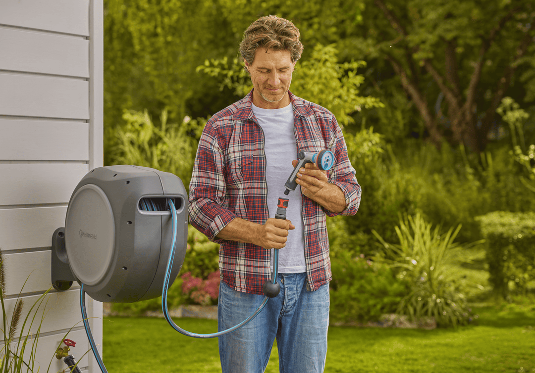 Retractable garden hose reel with gray reel and blue hose, nozzle held by person