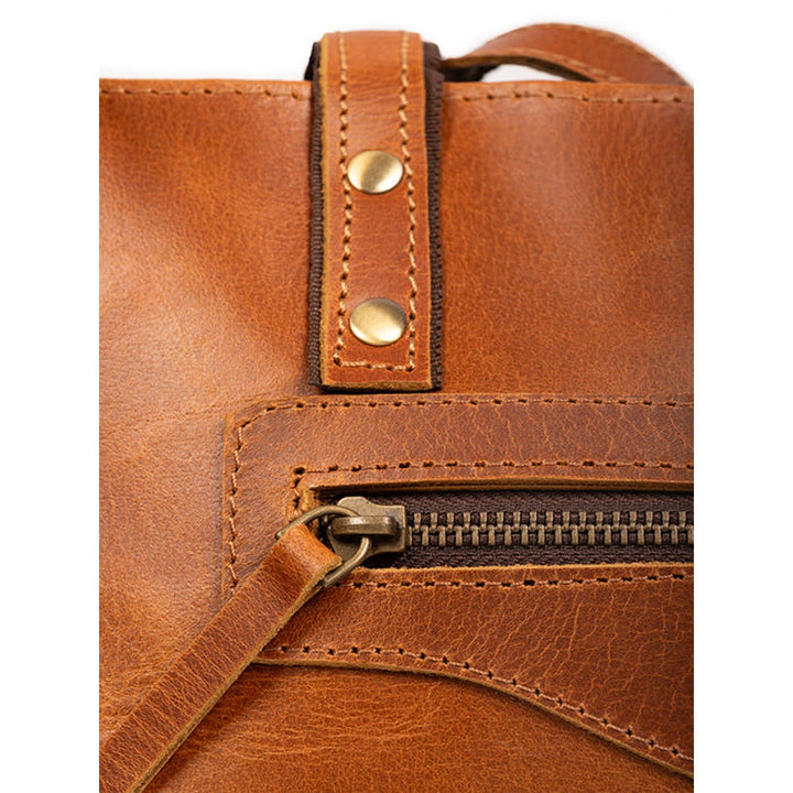 Tan leather tote bag zipper close-up with snap-tab detail and stitching