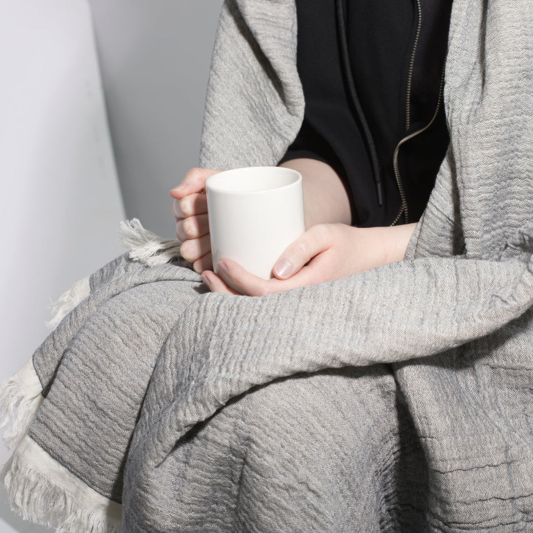 Grey muslin throw blanket wrapped around a person holding a mug