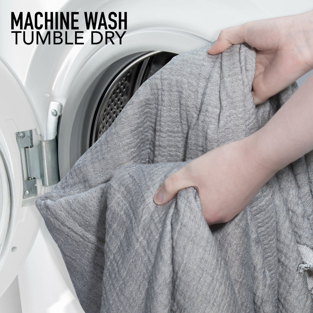 Grey muslin throw blanket being placed in a washing machine drum