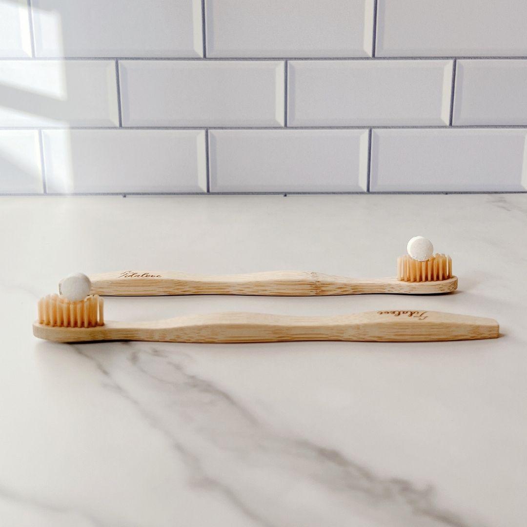 Two bamboo toothbrushes lying on a countertop, showing bristle ends and handles